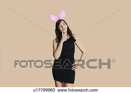 Thoughtful beautiful young woman with rabbit ears looking away over colored background View Large Photo Image Stock Image - Thoughtful beautiful young woman with rabbit ears looking away over colored background. Fotosearch