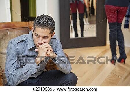 Thoughtful young man sitting with girlfriend in background View Large Photo Image Stock Photography - Thoughtful young man sitting with girlfriend in background. Fotosearch