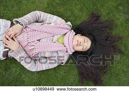Stock Photo - Top view of young Asian woman with long black hair lying on lawn. Fotosearch