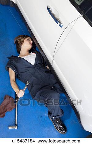 Woman lying down on floor working on car in automobile garage View Large Photo Image Picture - Woman lying down on floor working on car in automobile garage. Fotosearch