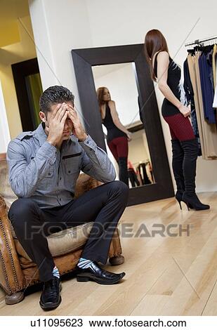 Worried young man sitting on armchair with woman in background trying on clothes View Large Photo Image Stock Image - Worried young man sitting on armchair with woman in background trying on clothes. Fotosearch