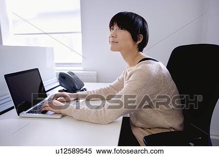 Young Asian woman using laptop while looking away View Large Photo Image Stock Photography - Young Asian woman using laptop while looking away. Fotosearch