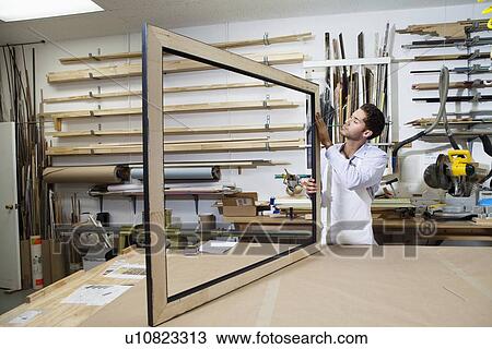 Stock Image - Young craftsman concentrating on making picture frame in workshop. Fotosearch