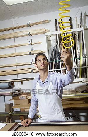 Stock Photograph - Young craftsman holding equipment in frame workshop. Fotosearch