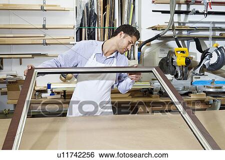 Stock Photograph - Young craftsman looking at picture frame. Fotosearch