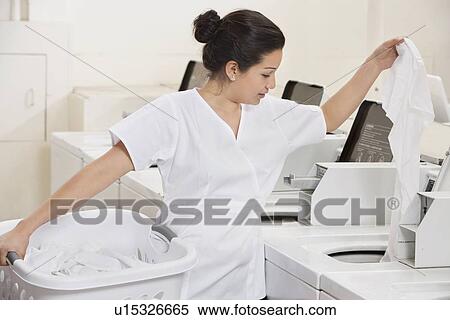 Young female employee putting clothes in washing machine View Large Photo Image Stock Photography - Young female employee putting clothes in washing machine. Fotosearch