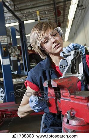 Stock Image - Young female mechanic in protective workwear working on machinery part in automobile repair shop. Fotosearch