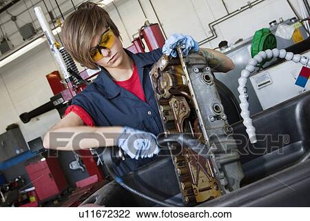 Stock Image - Young female mechanic working with welding torch on vehicle machinery part in auto repair shop. Fotosearch