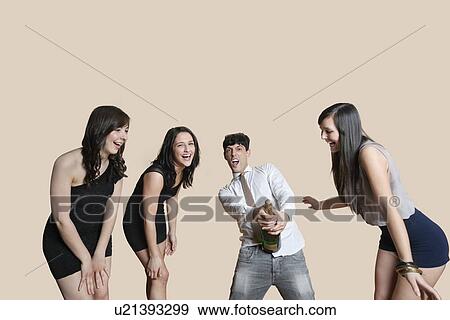 Young friends opening champagne bottle over colored background View Large Photo Image Stock Photo - Young friends opening champagne bottle over colored background. Fotosearch