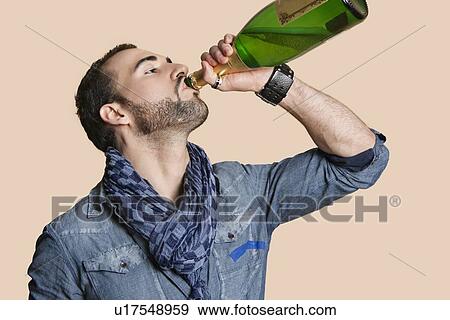 Stock Photo - Young man drinking champagne from bottle over colored background. Fotosearch