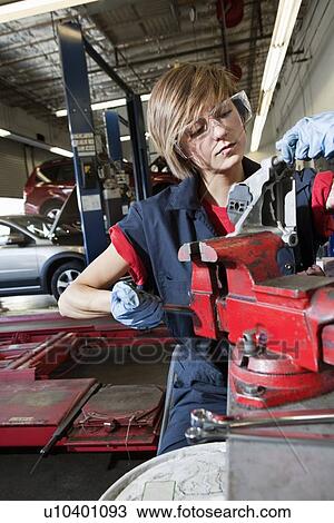 Stock Image - Young mechanic in protective clothing concentrating on repairing machine part in garage. Fotosearch