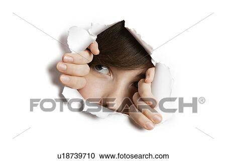 Stock Image - Young Middle eastern woman peeking from ripped white paper hole. Fotosearch