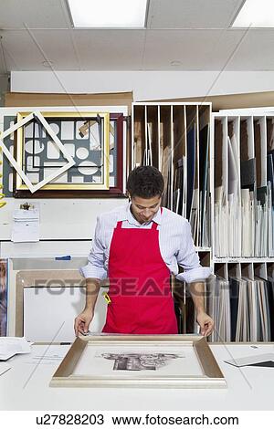 Stock Image - Young skilled worker adjusting frame on photograph. Fotosearch