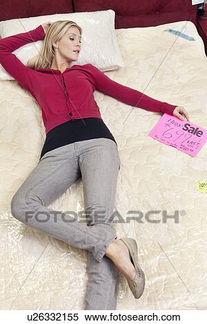 Stock Photography - Young woman lying on new mattress in furniture store. Fotosearch