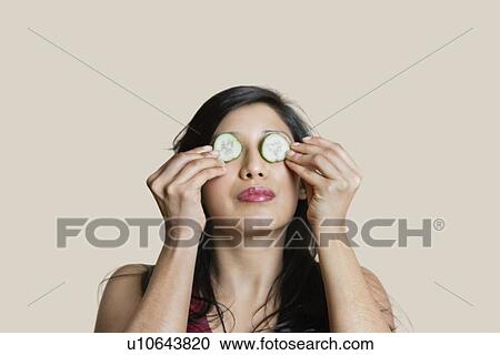 Stock Image - Young woman placing cucumber on eyes over colored background. Fotosearch