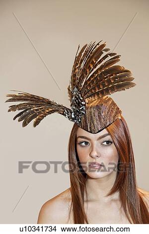 Young woman wearing feathered headdress while looking away over colored background View Large Photo Image Picture - Young woman wearing feathered headdress while looking away over colored background. Fotosearch