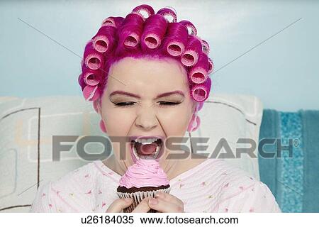 Stock Photography - Young woman with open mouth holding cupcake. Fotosearch