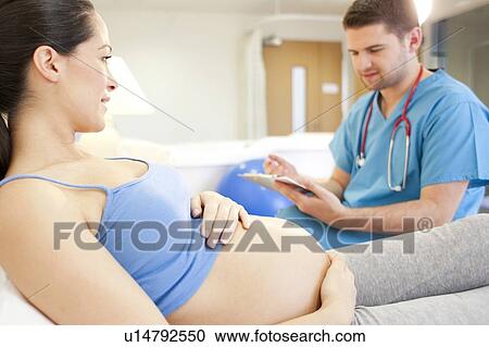 Stock Image - Birthing centre. Midwife checking on a pregnant woman in a room at a birthing centre.. Fotosearch