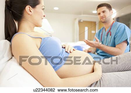 Stock Image - Birthing centre. Midwife checking on a pregnant woman in a room at a birthing centre.. Fotosearch