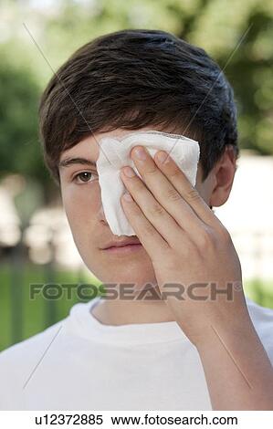 Stock Photography - Eye injury. Boy holding a sterile dressing over his injured eye.. Fotosearch