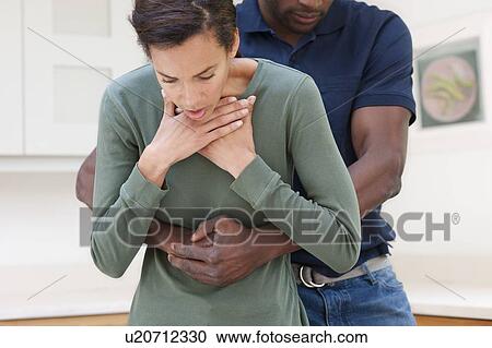 Stock Image - Heimlich manoeuvre. Man performing the Heimlich manoeuvre on a choking woman.. Fotosearch