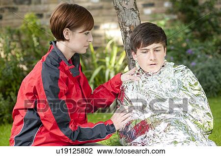 Stock Image - Hypothermia. Woman wrapping a boy in a foil blanket to warm him up.. Fotosearch