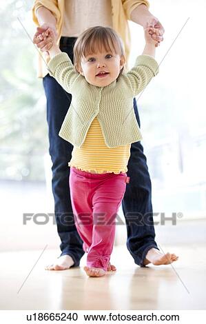 Stock Image - Learning to walk. Mother helping her 15 month old daughter to walk.. Fotosearch