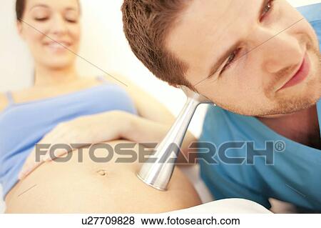 Stock Photo - Obstetric examination. Midwife using a pinard to listen to a foetus' heartbeat at a birthing centre.. Fotosearch