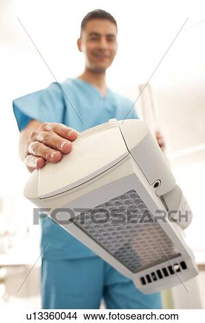 Picture - Photodynamic therapy. Dermatologist positioning a photodynamic therapy lamp over a patient.. Fotosearch