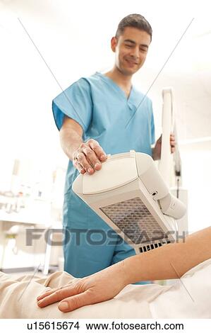 Picture - Photodynamic therapy. Dermatologist positioning a photodynamic therapy lamp over a patient.. Fotosearch