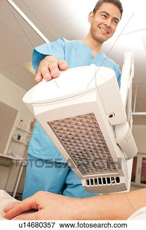Stock Photo - Photodynamic therapy. Dermatologist positioning a photodynamic therapy lamp over a patient.. Fotosearch
