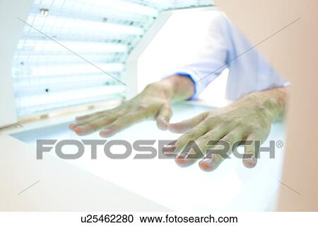 Stock Image - Phototherapy booth. Patient with their hands in a phototherapy box.. Fotosearch