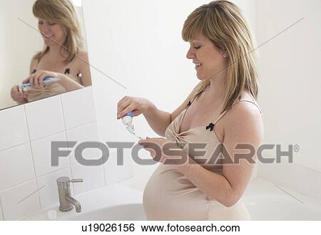 Stock Photograph - Pregnant woman brushing her teeth. She is 35 weeks pregnant.. Fotosearch