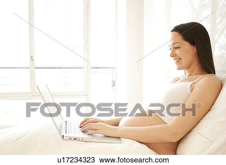 Pregnant woman using a laptop in bed. View Large Photo Image Stock Image - Pregnant woman using a laptop in bed.. Fotosearch