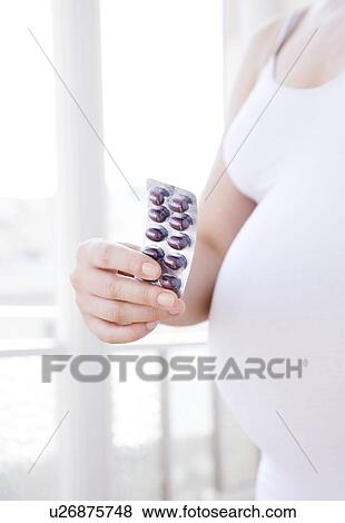 Stock Photo - Prenatal vitamins. Pregnant woman holding a packet of vitamins. She is eight and a half months pregnant.. Fotosearch