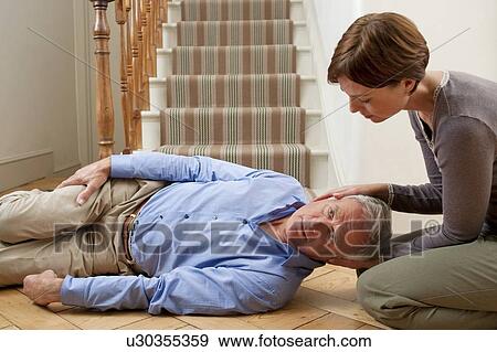 Stock Photo - Senior man injured in a fall being placed in the recovery position.. Fotosearch