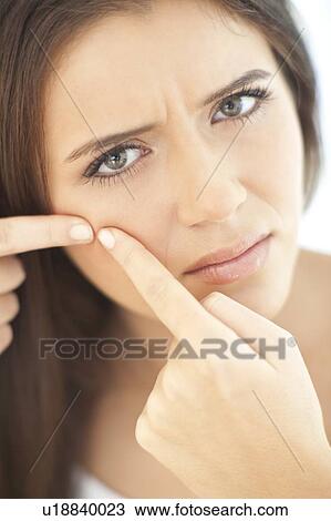 Stock Image - Squeezing spot. Teenage girl squeezing a spot on her face.. Fotosearch