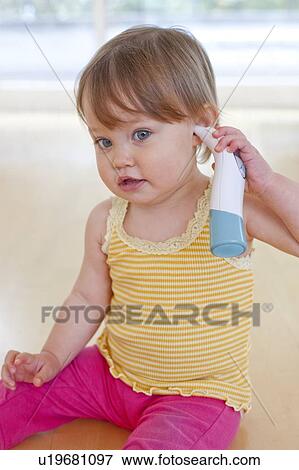 Toddler playing with thermometer. 15 month old girl taking her own temperature with an ear thermometer. View Large Photo Image Stock Photo - Toddler playing with thermometer. 15 month old girl taking her own temperature with an ear thermometer.. Fotosearch