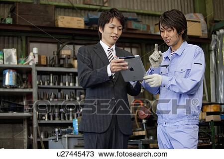 Stock Image - Businessman and Manual Worker Looking at Digital Tablet. Fotosearch