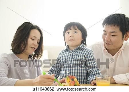 Stock Image - Family eating cake in living room. Fotosearch