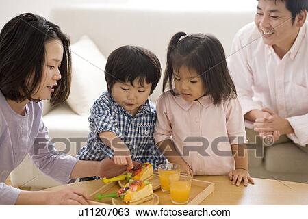 Stock Image - Family eating cake in living room. Fotosearch
