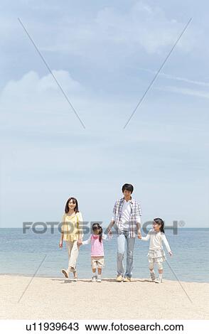 Stock Image - Family of Four Walking In Hand In Hand on Beach. Fotosearch