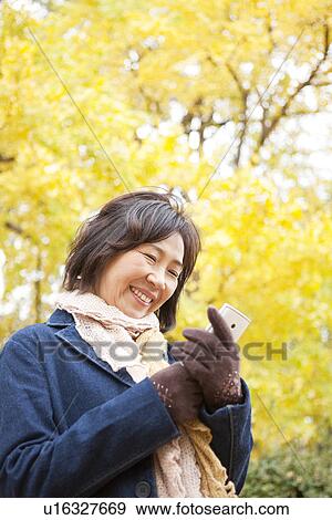 Stock Photo - Mature Woman Using Mobile Phone Outdoors In Autumn. Fotosearch