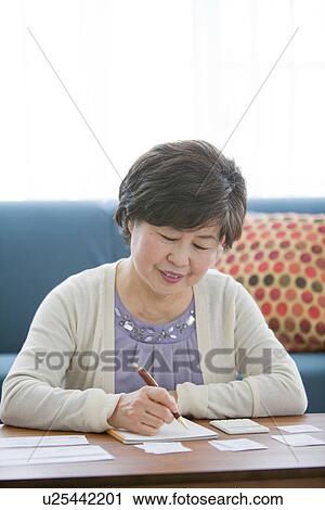 Stock Image - Mature Woman Writing In Living Room. Fotosearch