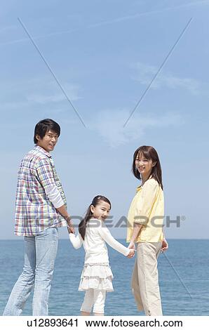 Stock Image - Parents and Daughter Standing on Beach. Fotosearch