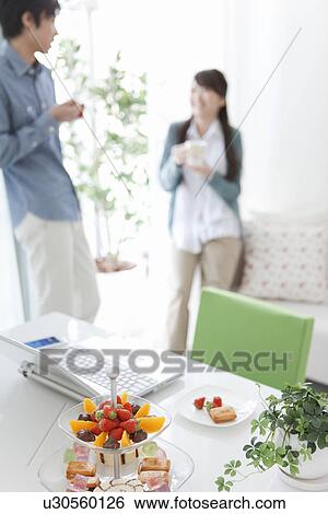 Stock Photograph - Snacks on Table, Young Couple In Background. Fotosearch