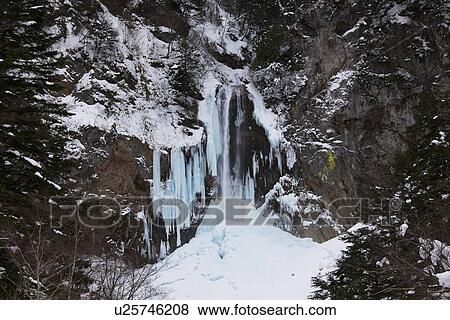 Stock Photo - Snowcapped cliff and freezing waterfall. Fotosearch