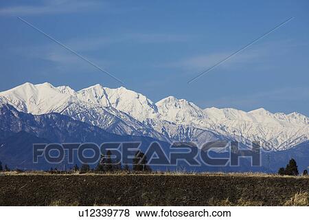 Stock Photo - Snowcapped mountain chain behind rural landscape. Fotosearch