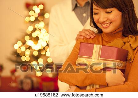 Stock Image - Woman Holding Christmas Present, Man Touching Shoulders. Fotosearch