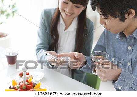Stock Photo - Young Couple Using Mobile Phone and Having Drink. Fotosearch